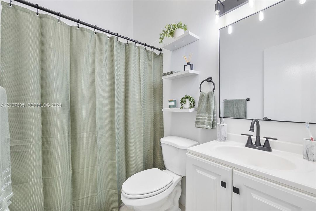 Bathroom featuring a white vanity with a rectangular sink, matte black faucet, wall-mounted light fixture with glass shades, frameless mirror, and built-in shelving