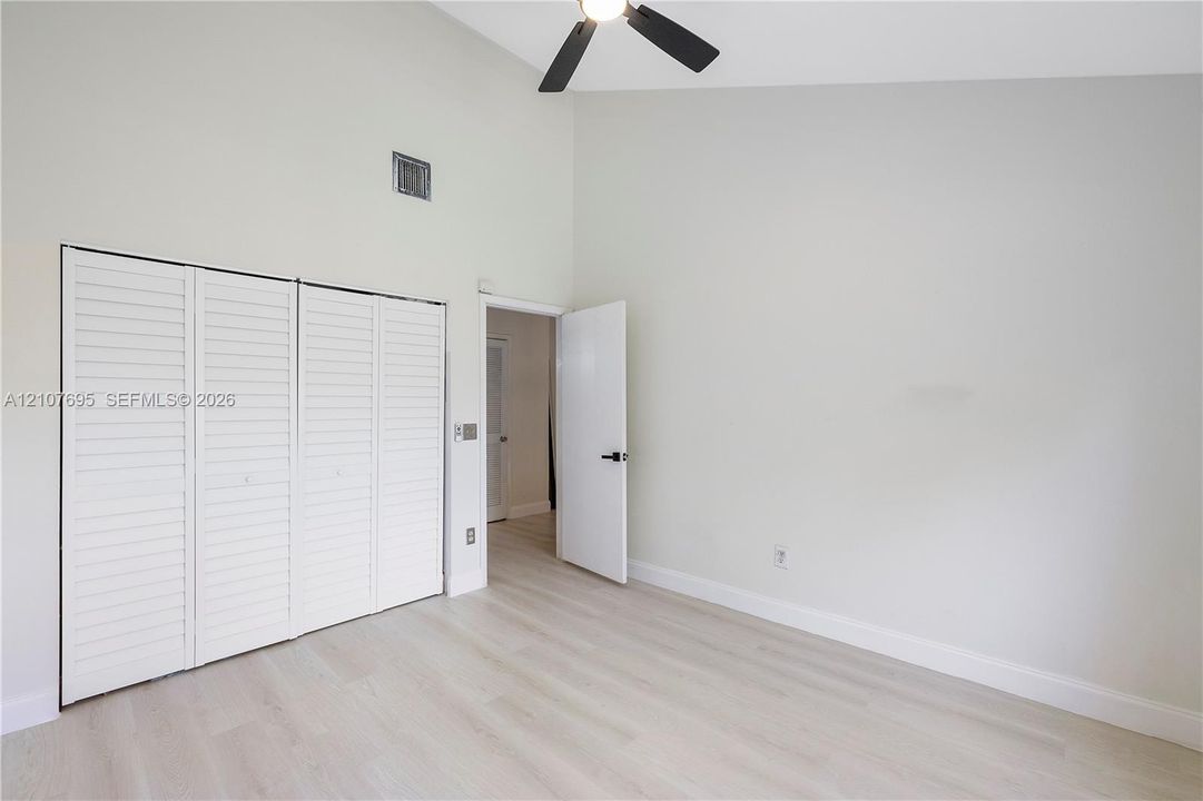 Vaulted ceilings, wood-finish flooring, four-panel louvered closet doors, and a ceiling-mounted light fixture
