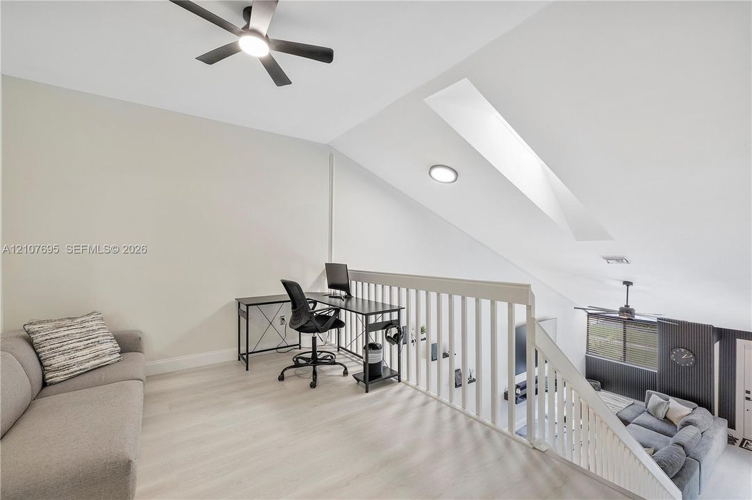 Open loft area featuring vaulted ceilings, a skylight, wood-finish flooring, and a ceiling fan with integrated lighting