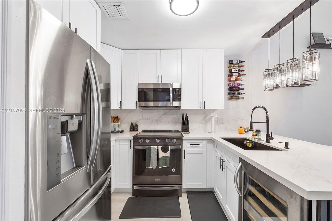 Kitchen featuring white shaker-style cabinetry, white countertops with grey veining, stainless steel appliances, a black undermount sink with a gooseneck faucet, and multi-pendant overhead lighting