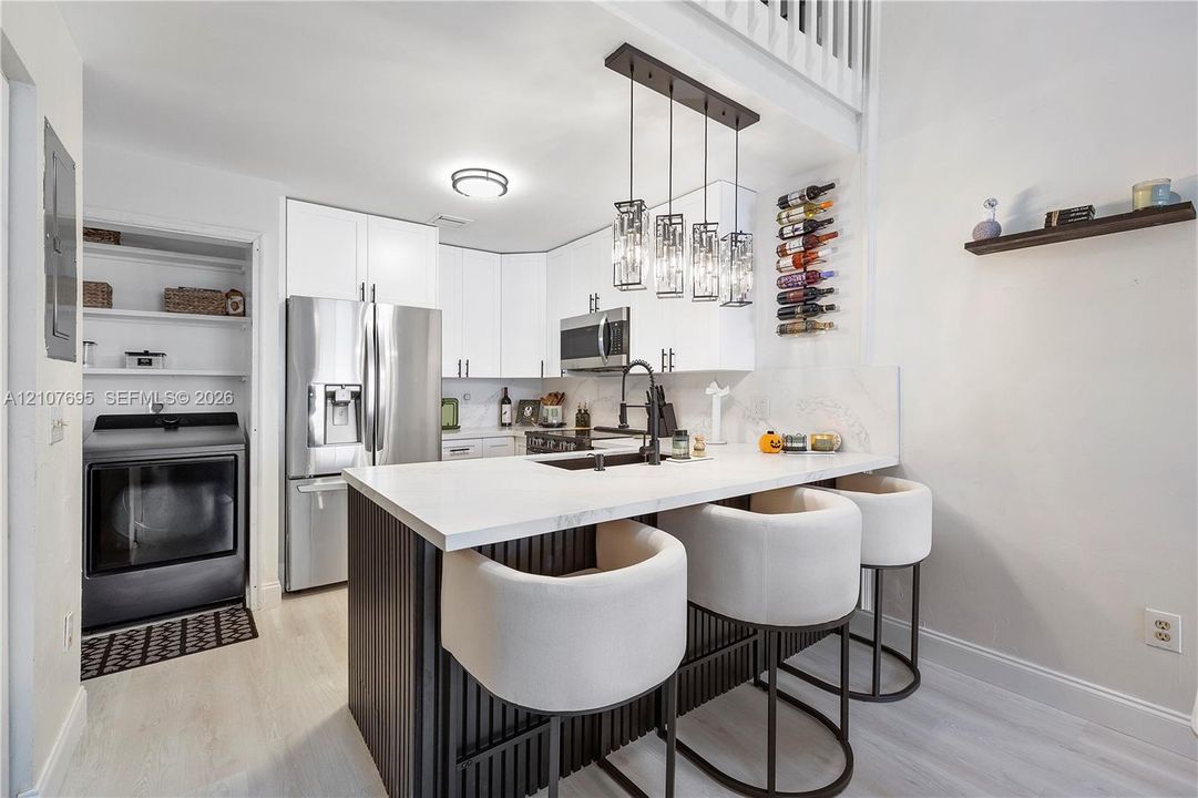 Kitchen featuring white cabinetry, an island with a waterfall-edge countertop, matte black fixtures, stainless steel appliances, and a built-in wine rack