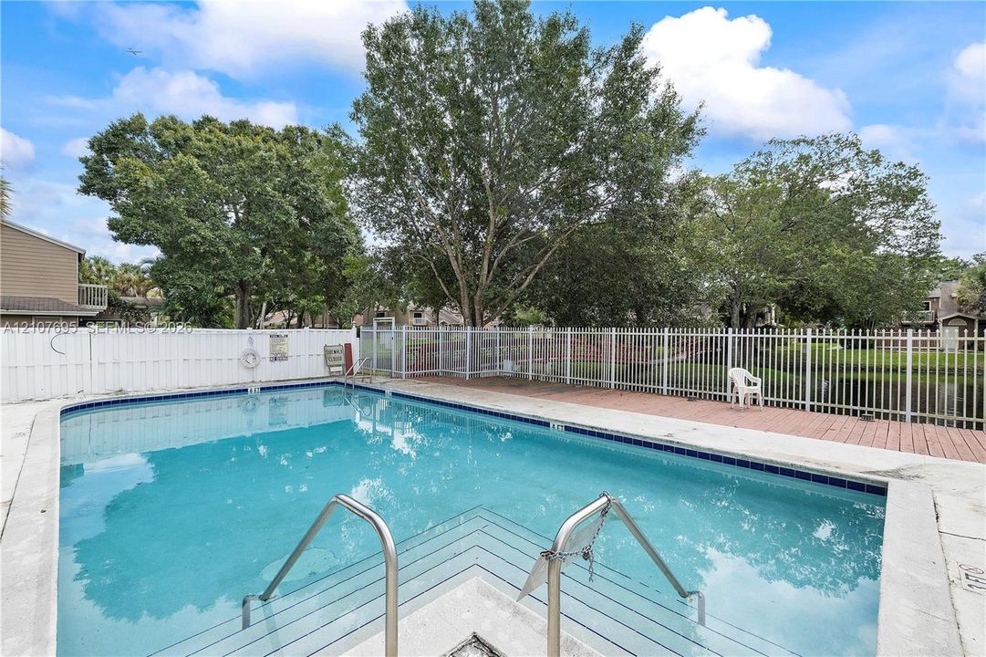 Swimming pool featuring a concrete deck, metal railings, and a white privacy fence