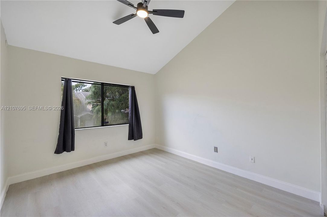 Vaulted ceiling, light-tone wood-finish flooring, and matte black ceiling fan