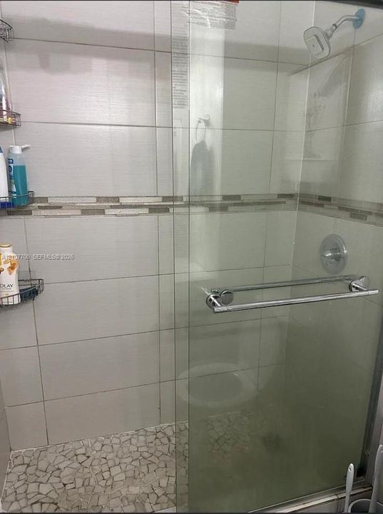 Walk-in shower featuring a glass enclosure, pebble-stone flooring, large-format tile surround, decorative accent inlay, and polished chrome hardware