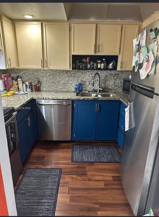 Kitchen featuring two-tone cabinetry, stone countertops, stainless steel appliances, a dual-basin undermount sink, and wood-finish flooring