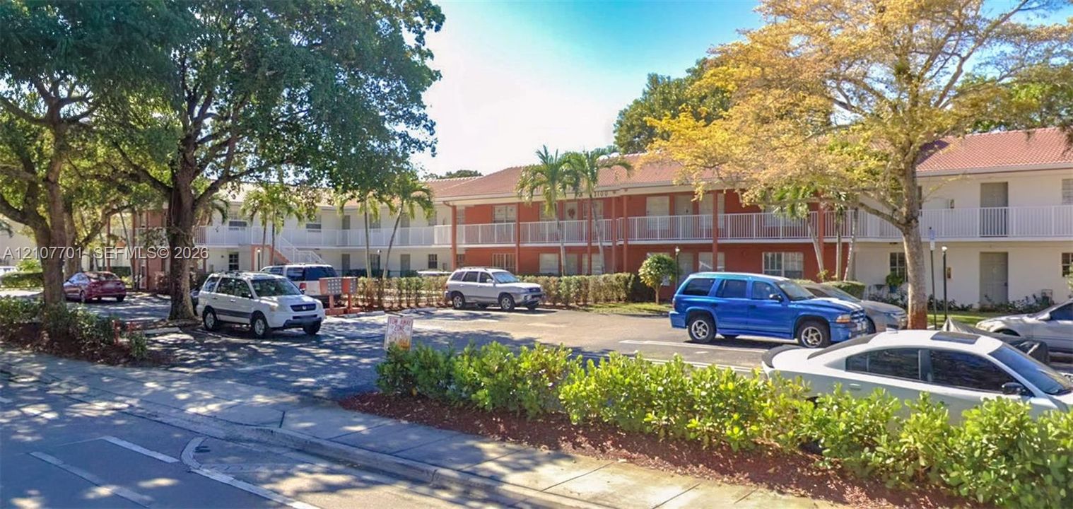 Multi-story exterior featuring a tile roof, white balcony railings, and lush landscaping with mature trees