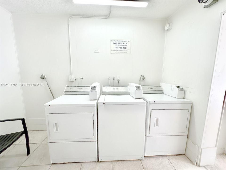 Laundry area featuring three white top-loading washers and light-toned tile flooring