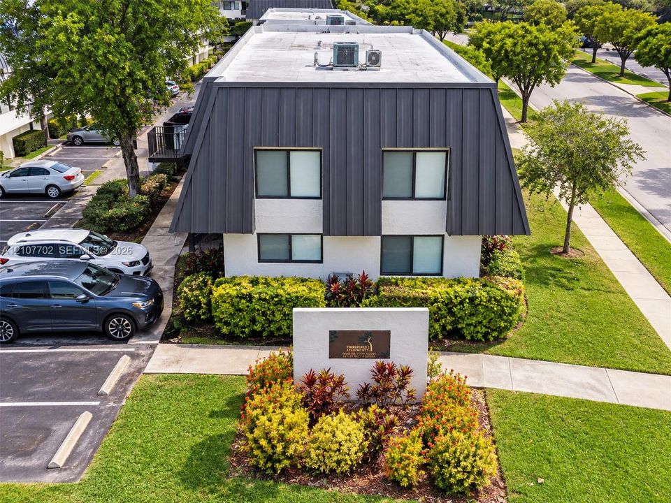 Exterior featuring a mansard roof, stucco facade, onsite parking, concrete sidewalks, and manicured shrubbery