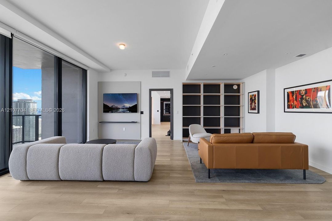 Open-concept living space featuring wood-finish flooring, floor-to-ceiling glass sliding doors, built-in floor-to-ceiling shelving, and a wall-mounted media console