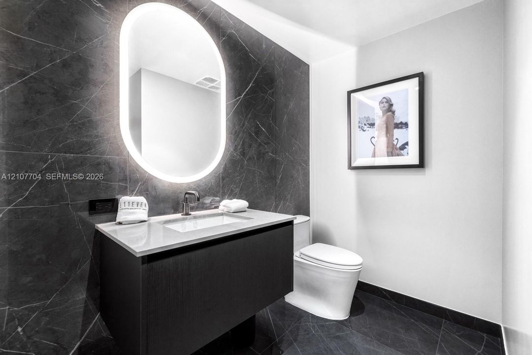 Floating vanity with a light-toned countertop, dark stone-finish wall tile, integrated oval back-lit mirror, and modern wall-mounted faucet