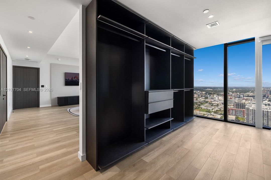 Custom-built dark finish storage cabinetry featuring integrated drawers and hanging rods, light-toned wood-finish flooring, and floor-to-ceiling windows