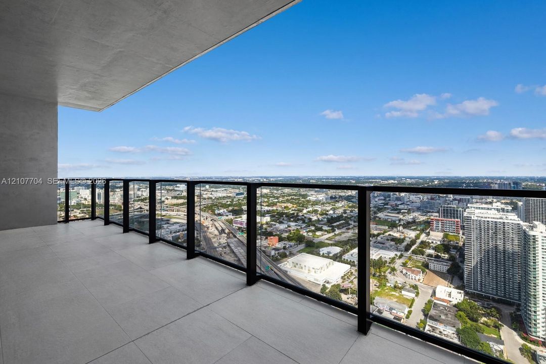 Covered balcony featuring large-format stone-finish tiling and a black-framed glass railing