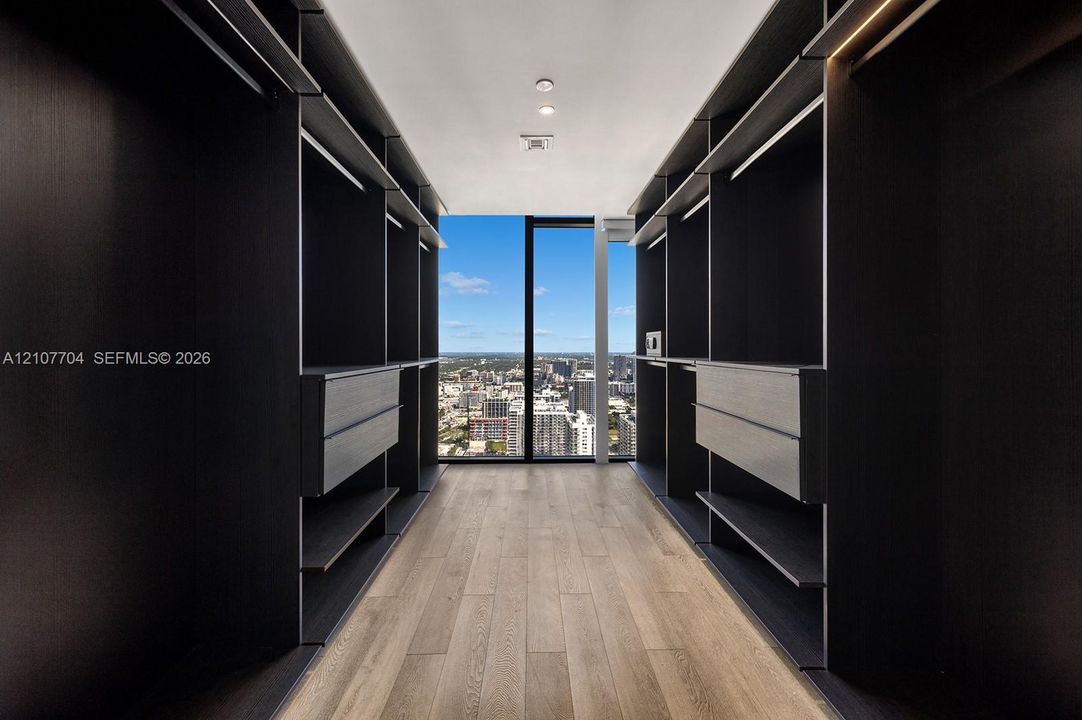Custom walk-in closet featuring floor-to-ceiling dark cabinetry, integrated shelving, drawer units, wood-finish flooring, and full-height window panels
