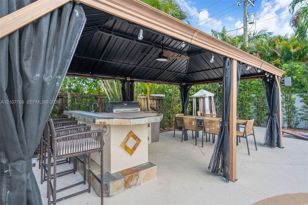 Outdoor pavilion featuring a metal roof, built-in bar with stone-tile detailing, stainless steel grill, and ceiling fan