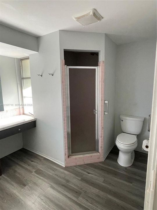 Bathroom featuring wood-finish flooring, a floating vanity with a neutral-toned countertop, a glass-enclosed shower with decorative tile surround, and a wall-mounted toilet