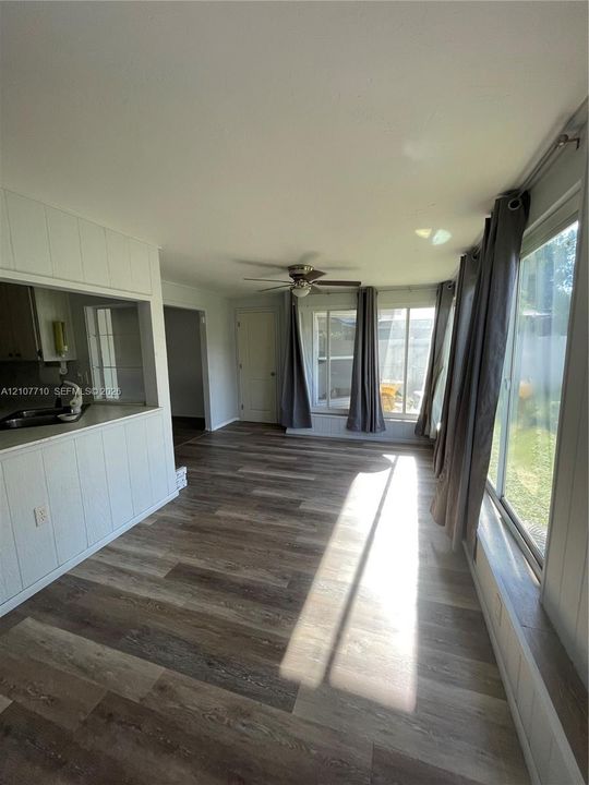 Wood-finish flooring, vertical wood paneled walls, ceiling fan, and large windows with built-in ledges