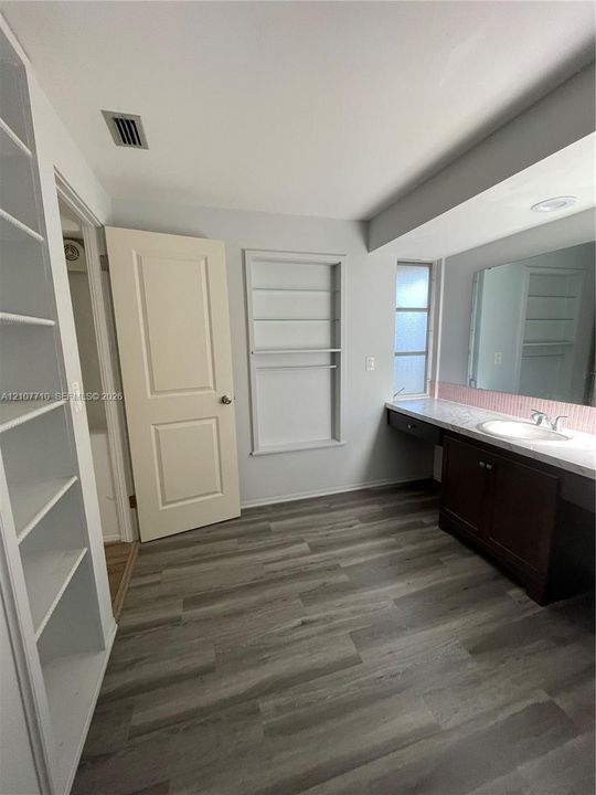 Wood-finish flooring, built-in shelving, dark wood vanity with a solid surface countertop, integrated sink, and large wall-mounted mirror