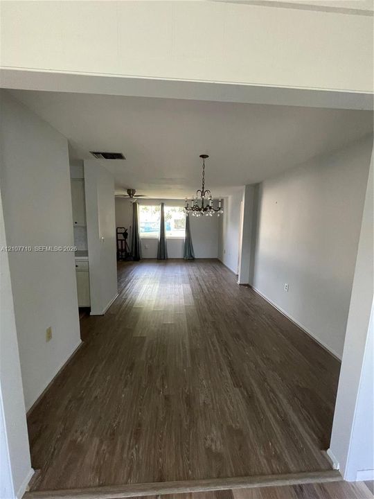 Open-concept interior featuring wood-finish flooring, a multi-arm crystal chandelier, and large windows