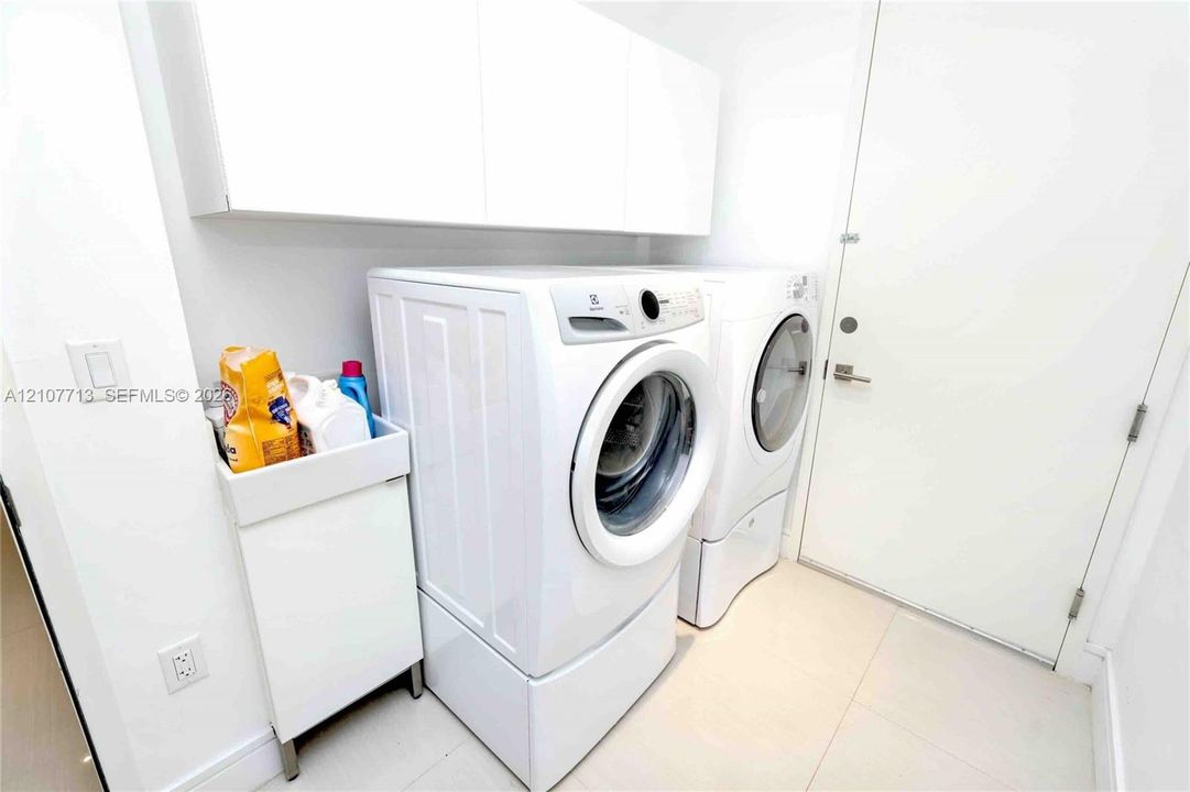 Laundry area featuring minimalist white cabinetry, built-in utility sink, and large-format tile flooring