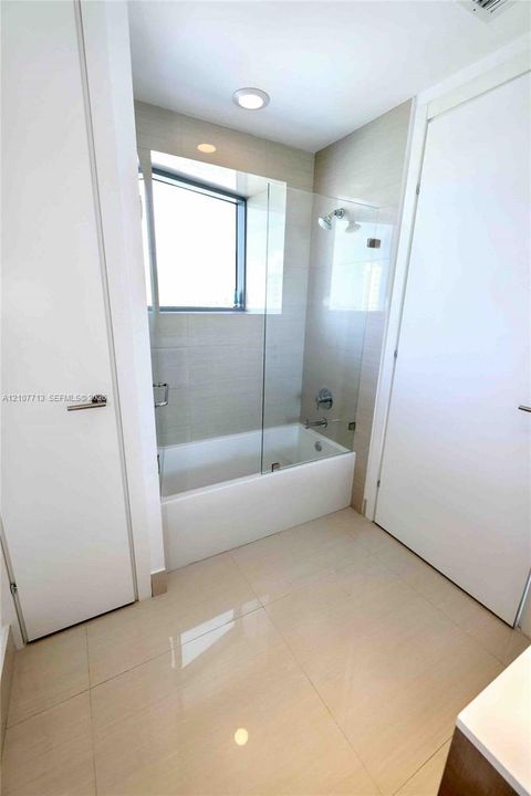 Bathroom featuring large-format tile flooring, a soaking tub with a glass panel screen, recessed lighting, and a neutral wall-tile surround