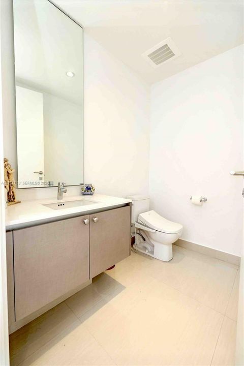 Floating vanity with a light-toned countertop, rectangular undermount sink, chrome faucet, expansive wall-mounted mirror, and large-format tile flooring