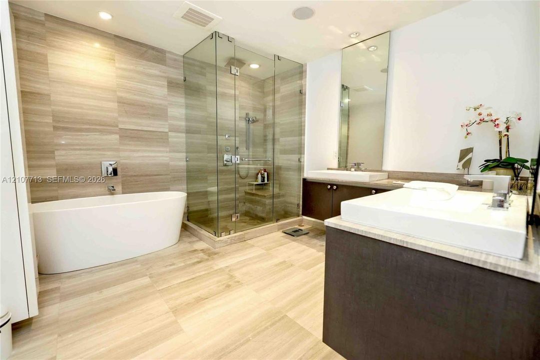 Freestanding soaking tub, glass-enclosed walk-in shower with tiled surround, dual-sink vanity with solid-surface countertops, and oversized wall mirror