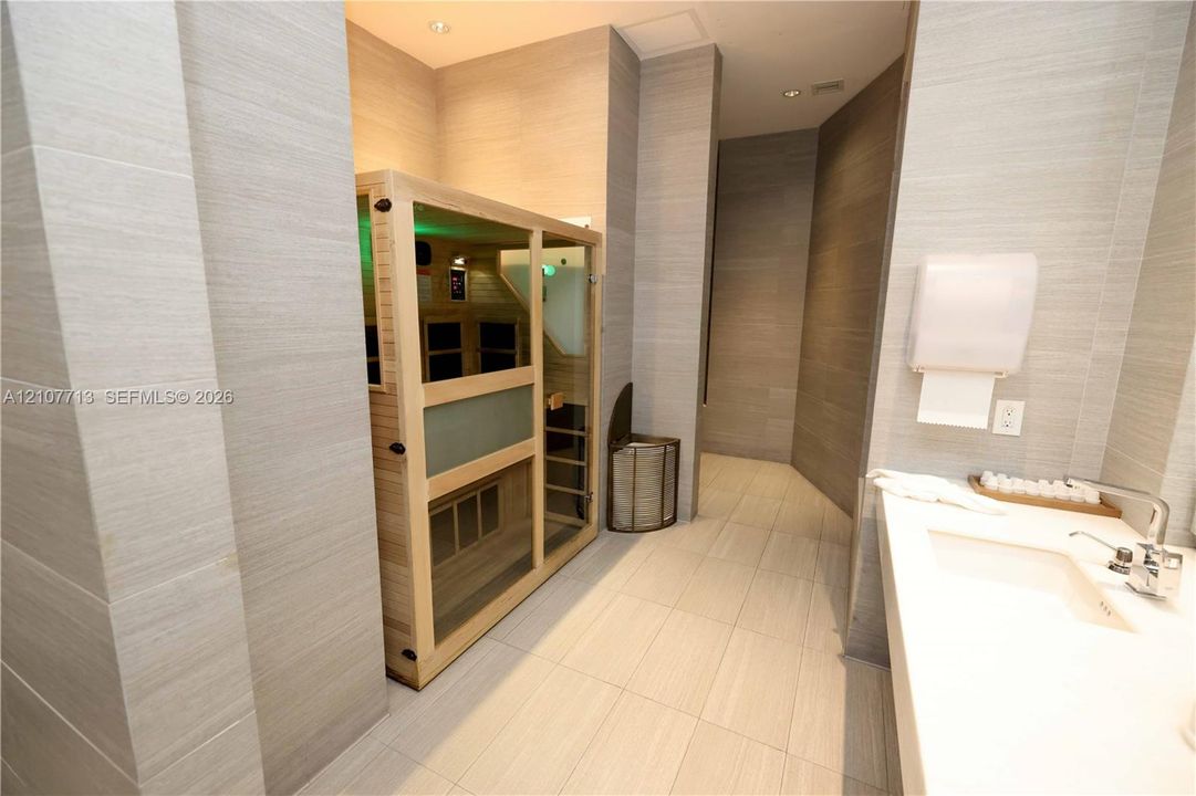 Enclosed wood-frame sauna, full-height wall tiling, recessed lighting, and rectangular integrated sink with chrome-finish faucet