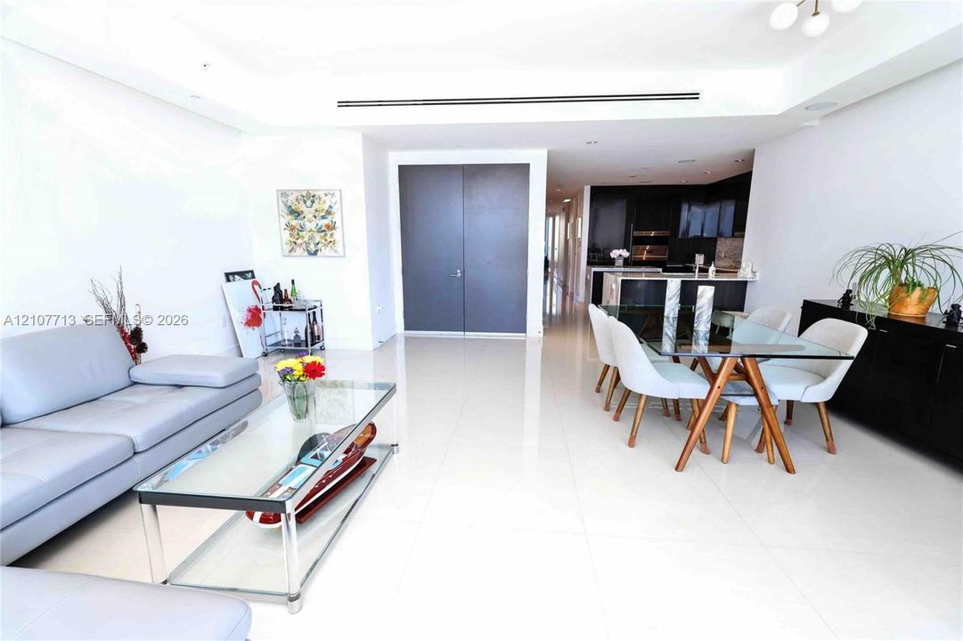 Open-concept interior featuring polished tile flooring, recessed tray ceiling, high-contrast cabinetry, and double-door entry