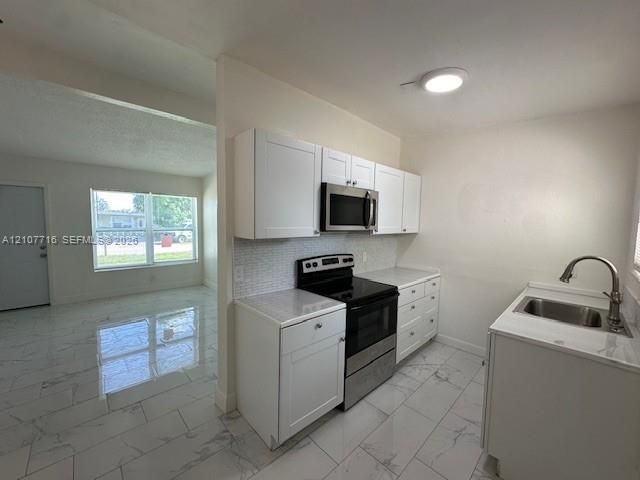 Kitchen featuring white shaker-style cabinetry, stainless steel appliances, a tile backsplash, and light-toned tile flooring throughout