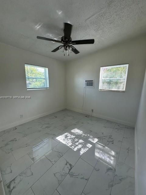 Interior space featuring large-format stone-finish floor tiling, dual windows, a ceiling fan with integrated lighting, and a wall-mounted air conditioning unit