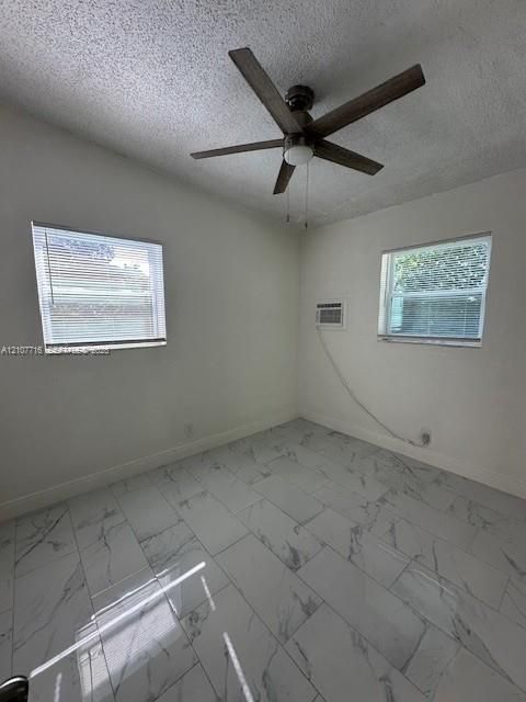 Interior space featuring white stone-finish tile flooring, dual windows, a five-blade ceiling fan, and a wall-mounted cooling unit