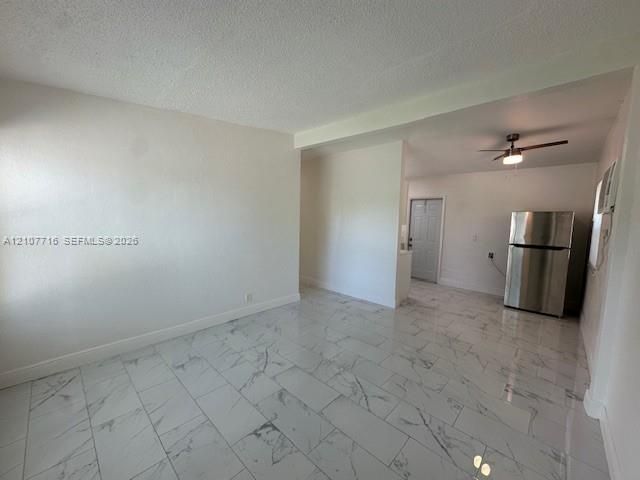Large-format stone-look tile flooring with a neutral veining pattern, stainless steel refrigerator, and ceiling fan with integrated lighting