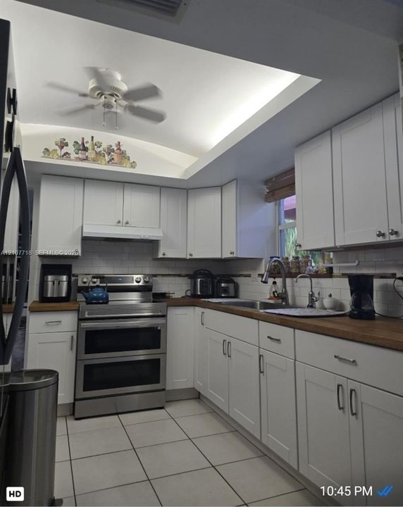 White cabinetry with shaker-style doors, wood-finish countertops, stainless steel dual-oven range, subway tile backsplash, and recessed tray ceiling with integrated lighting