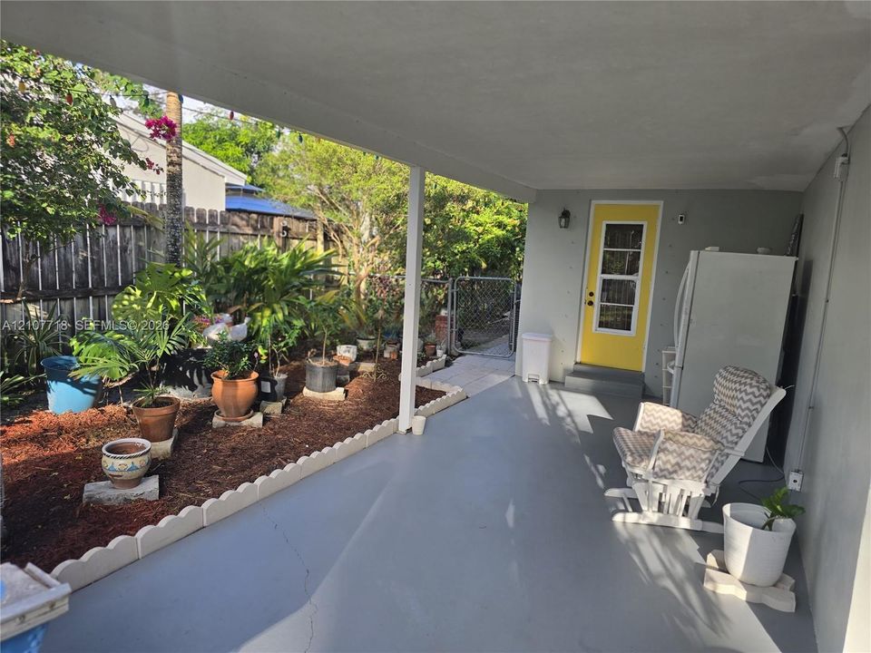 Covered concrete patio featuring a scalloped concrete landscape border, wood-mulch garden bed, and a exterior door with a multi-pane glass insert