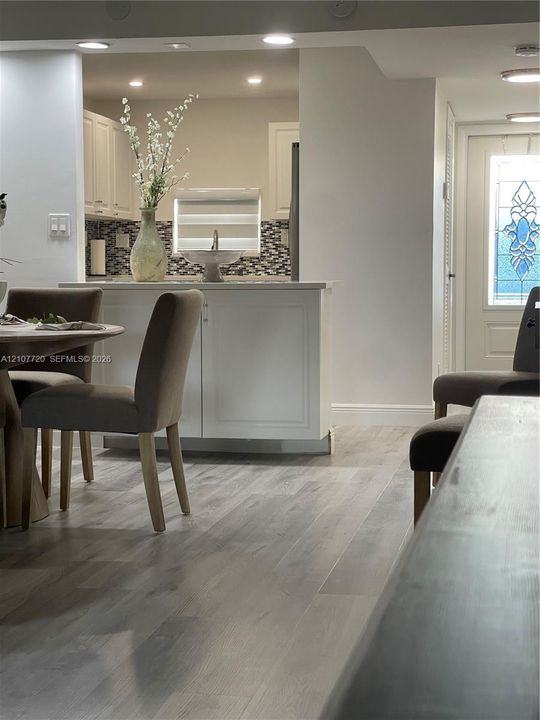 Kitchen featuring a peninsula with built-in cabinetry, stone-tiled backsplash, recessed lighting, and wood-finish flooring, including a front entry door with decorative glass inlay