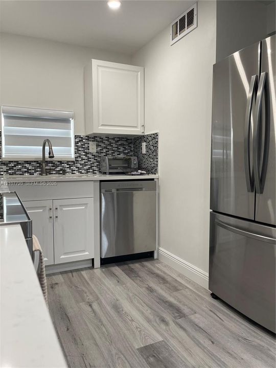 Kitchen featuring white shaker-style cabinetry, wood-finish flooring, stainless steel appliances, and a mosaic tile backsplash