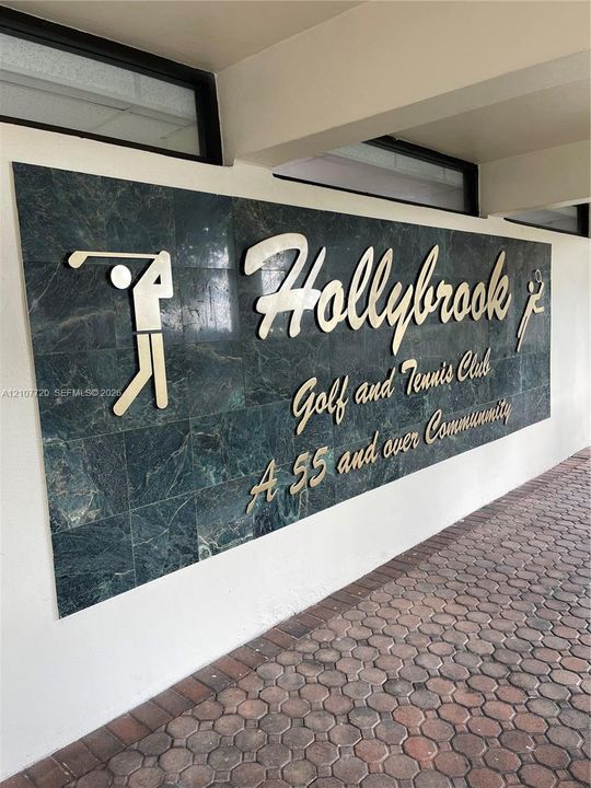 Stone-tiled signage featuring metallic lettering and integrated golf and tennis iconography, set against a paved brick walkway