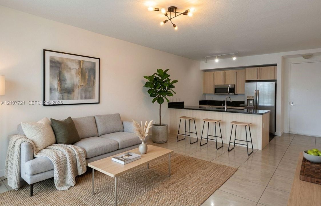 Open-concept interior featuring light-toned cabinetry, dark stone countertops, stainless steel appliances, ceramic tile flooring, and a modern multi-bulb ceiling fixture