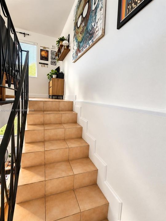 Staircase featuring ceramic tile treads, white wainscoting, and a geometric metal railing