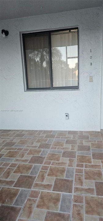 Covered exterior entryway featuring textured white stucco walls, multi-tonal decorative tile flooring, and a single-pane sliding window