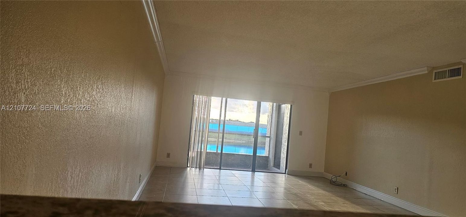 Living area featuring tile flooring, crown molding, and sliding glass doors opening to a balcony with water scenery