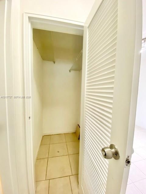 Storage space featuring a white louvered door, brushed metal hardware, and tiled flooring
