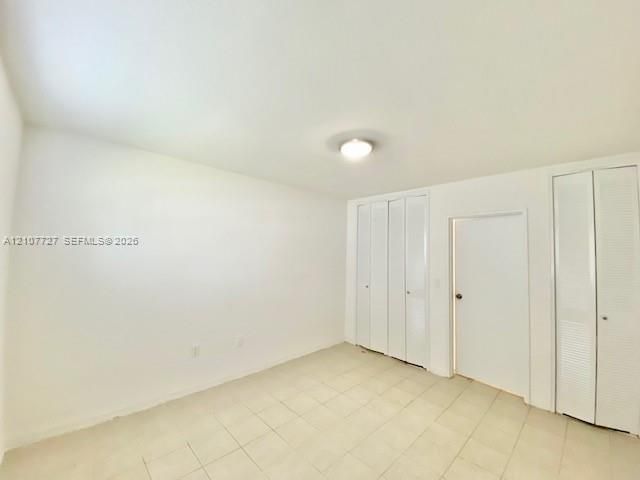 Interior room featuring neutral wall finishes, tile flooring, dual sets of bi-fold closet doors, and a central ceiling light fixture