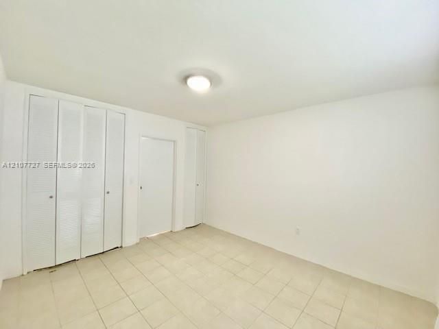 Room interior featuring neutral tile flooring, white walls, flush-mount ceiling lighting, and multiple floor-to-ceiling closets with white louvered bi-fold doors