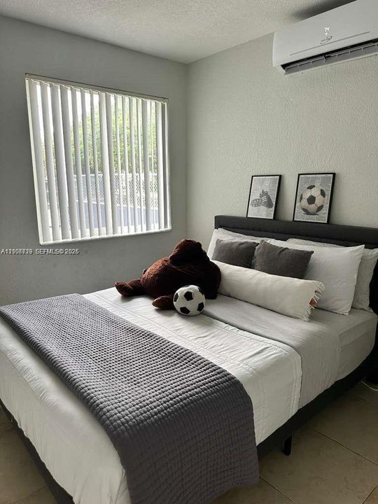 Wall-mounted ductless air conditioning unit, vertical window blinds, and neutral tile flooring