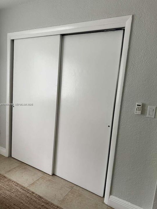 Sliding closet doors featuring white panels, neutral textured wall finish, and neutral tile flooring