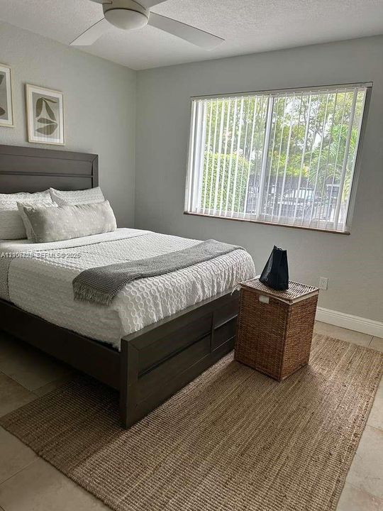 Neutral-toned room featuring a white ceiling fan with integrated lighting, a large window with vertical blinds, and tile flooring