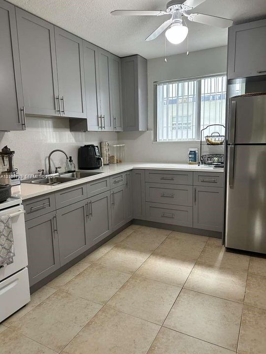 Kitchen featuring grey Shaker-style cabinetry, solid surface countertops, stainless steel undermount sink, porcelain tile flooring, and a ceiling-mounted light fixture
