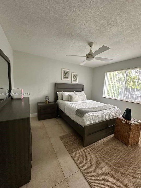Neutral-toned interior space featuring oversized tile flooring, a white ceiling fan, and large windows with vertical blinds