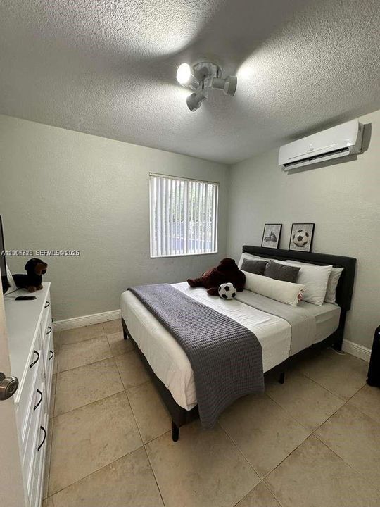 Interior space featuring large-format tile flooring, a wall-mounted ductless air conditioning unit, vertical window blinds, and a multi-directional track light fixture